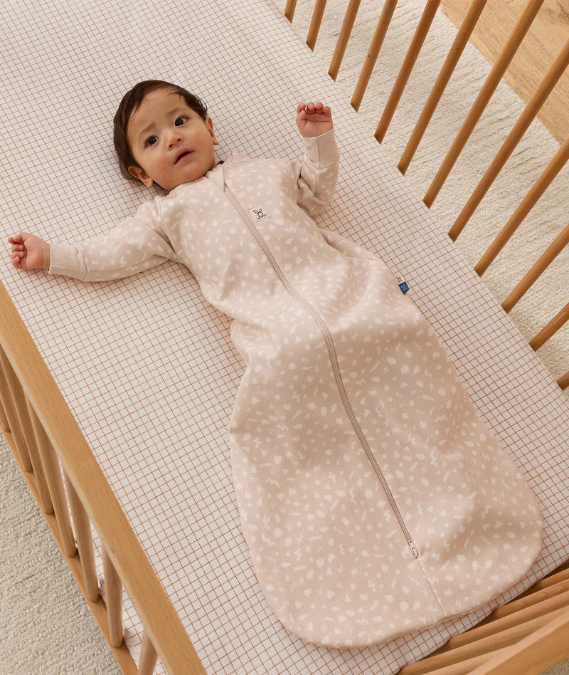 Infant dressed in a long-sleeve patterned Sleeping Bag 1.0 TOG, lying in a wooden cot