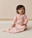 Infant sitting on a white mat, wearing a pink sleeved Sleeping Bag 1.0 TOG