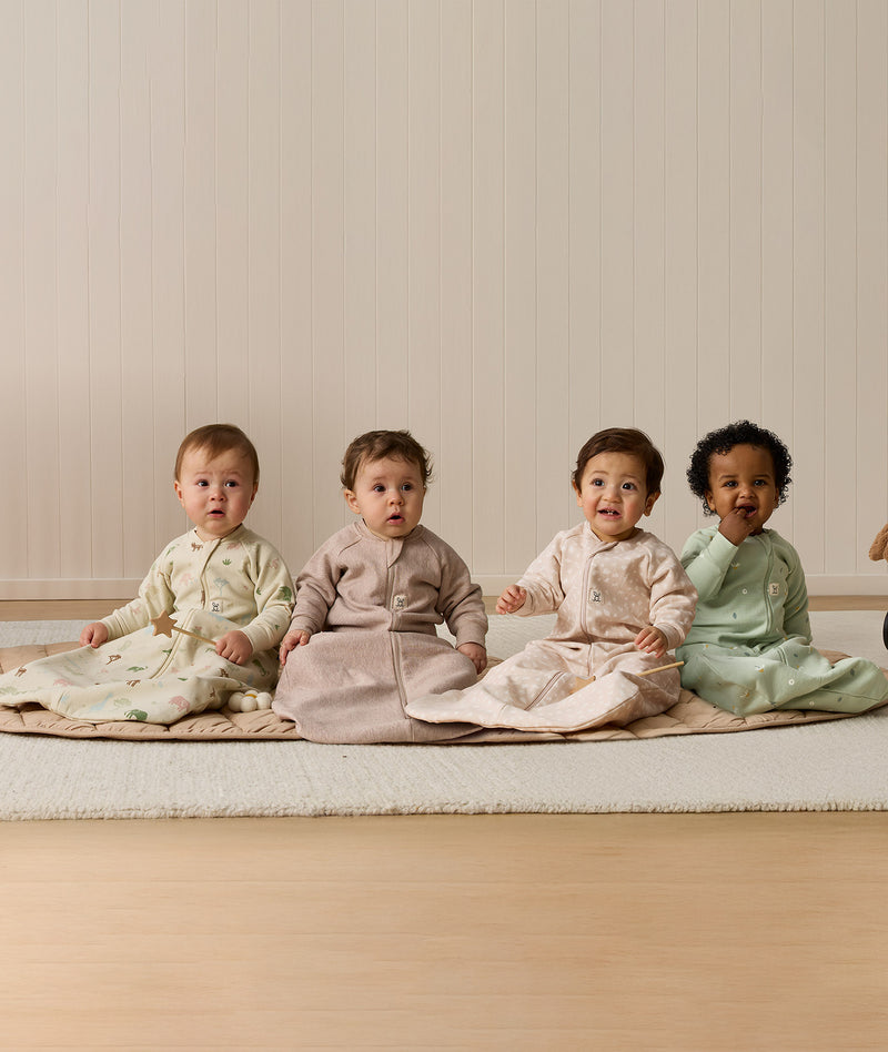 Four infants sitting side-by-side wearing ergoPouch Sleeping Bag 1.0 TOG Sleeved in Savannah, Taupe Marle, Coastal, and Meadow.
