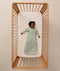 Infant lying inside a wooden cot with a grid-patterned sheet, wearing a long-sleeve Sleeping Bag 1.0 TOG