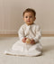 Infant sitting, wearing a sleeved Sleeping Bag 1.0 TOG Oatmeal Marle, while holding a wooden toy.
