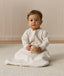 Infant sitting, wearing a sleeved Sleeping Bag 1.0 TOG Oatmeal Marle, while holding a wooden toy.