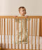 Infant standing inside a wooden cot wearing a long-sleeve sleeping bag