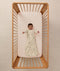 Overhead view of a baby lying on their back in a wooden cot, wearing a safari-patterned long-sleeve Sleeping Bag with arms outstretched.