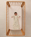 Overhead view of a baby lying on their back in a wooden cot, wearing a safari-patterned long-sleeve Sleeping Bag with arms outstretched.