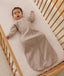 Infant lying in a cot, wearing an ergoPouch Sleeping Bag 1.0 TOG Sleeved Taupe Marle