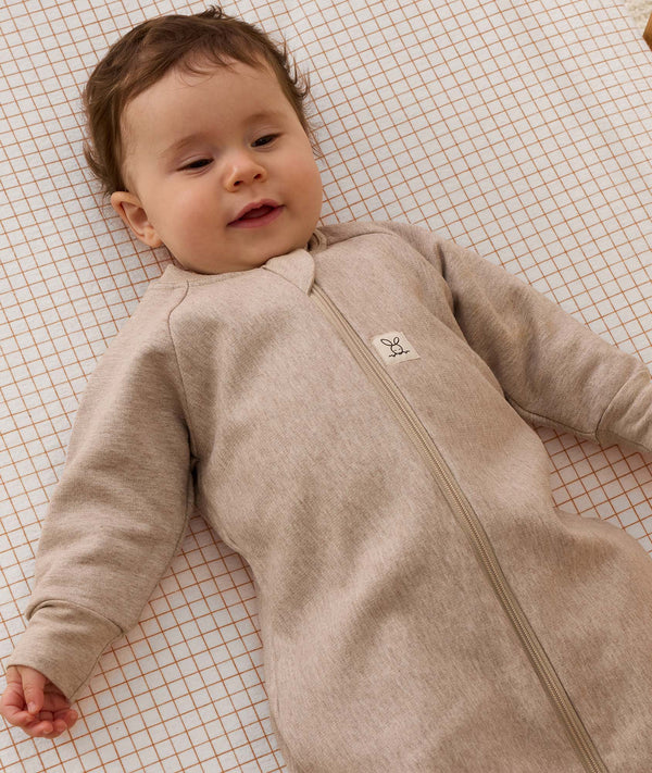 Infant lying on a grid-patterned  sheet, wearing a long-sleeve Sleeping Bag 1.0 TOG with front zip