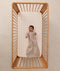 A happy baby lying in a wooden cot, wearing a sleeved Sleeping Bag 1.0 TOG Taupe Marle