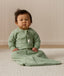 Infant sitting on a white mat, wearing a Sleeved Sleeping Bag 1.0 TOG Willow