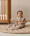 Smiling infant dressed in a sleeveless Sleeping Bag 1.0 TOG Taupe Marle, sitting on a quilted mat.