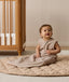 Smiling infant dressed in a sleeveless Sleeping Bag 1.0 TOG Taupe Marle, sitting on a quilted mat.