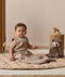 Infant wearing a sleeveless Sleeping Bag 1.0 TOG, sitting next to a plush toy on a quilted mat.