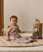 Infant wearing a sleeveless Sleeping Bag 1.0 TOG, sitting next to a plush toy on a quilted mat.