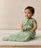 Infant sitting on a white mat, wearing a green Sleeping Bag 1.0 TOG