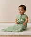 Infant sitting on a white mat, wearing a green Sleeping Bag 1.0 TOG