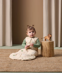 Infant sits on a rug, dressed in an ergoPouch 2.5 TOG Sleeping Bag with a Long Sleeve Layer underneath.