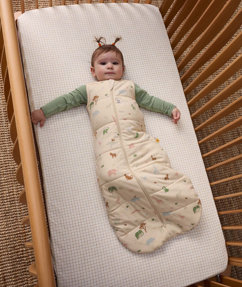 Baby lying in a cot, wearing an ergoPouch 2.5 TOG Sleeping Bag with a Long Sleeve Layer underneath.