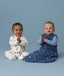 Two babies sitting on a light blue background, one wearing a white Long-Sleeve Layer with a colourful print and the other wearing a blue Long-sleeve layer with a matching blue Sleeping Bag.