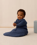 Baby sitting upright, wearing a blue Sleeping Bag 3.5 TOG with sleeves for extra warmth.