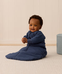 Baby sitting upright, wearing a blue Sleeping Bag 3.5 TOG with sleeves for extra warmth.