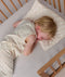 Overhead view of a toddler sleeping in a cot with their head resting on a matching patterned toddler pillow.