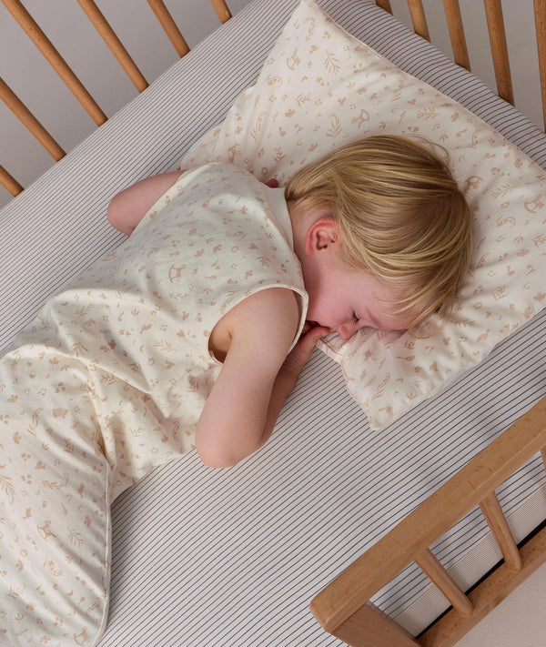 Overhead view of a toddler sleeping in a cot with their head resting on a matching patterned toddler pillow.