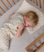 Overhead view of a toddler sleeping in a cot with their head resting on a matching patterned toddler pillow.