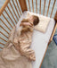 Toddler lying in a wooden cot with head resting on a low-profile toddler pillow.