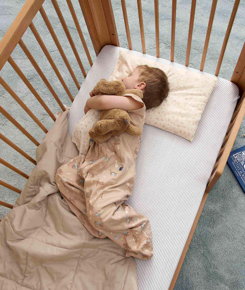 Toddler lying in a wooden cot with head resting on a low-profile toddler pillow.