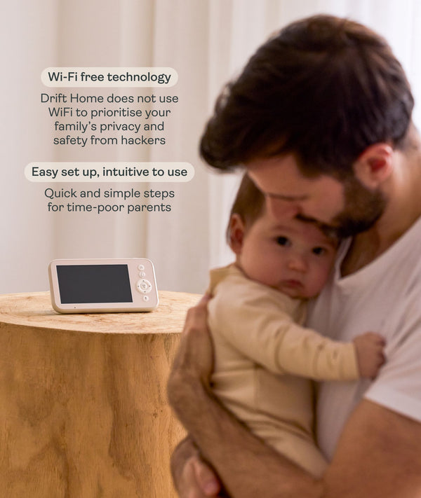 Drift Home Wi-Fi free baby monitor parent unit sitting on a wooden nightstand, with a father holding a baby in the background and text overlay highlighting privacy and easy setup features.