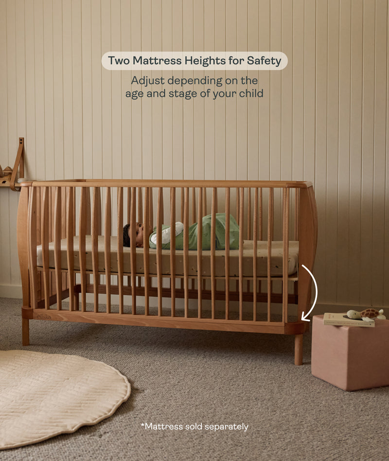 Wooden cot with mattress in a nursery setting, emphasizing safety and adjustability.