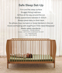 Wooden cot with a baby inside, set against a white curtain background.