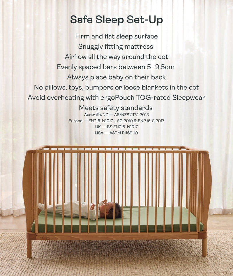 Wooden cot with a baby inside, set against a white curtain background.