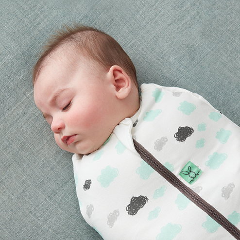 Newborn baby sleeping restfully on back, wearing a swaddle pouch