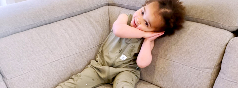 Toddler sitting on couch, resting side of face on closed balms, mimicking sleep position