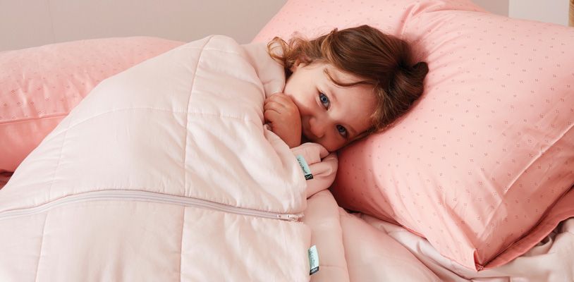 Toddler girl snuggling in big bed with pink ergoPouch bedding
